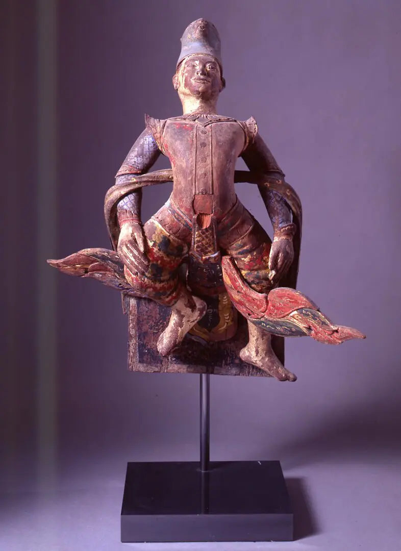 Figura do zodíaco em madeira policromada, sentada sobre uma ave de asas abertas, em suporte de metal