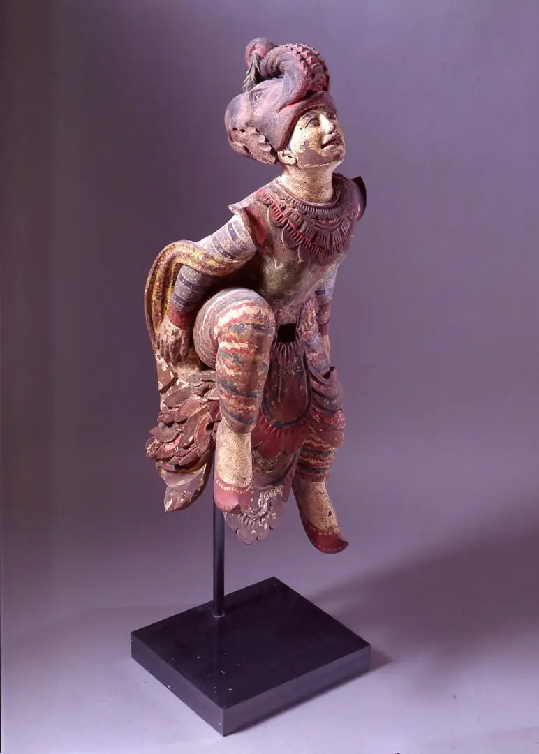 Figura do zodíaco em madeira policromada, com turbante e joelho levantado, em suporte de metal