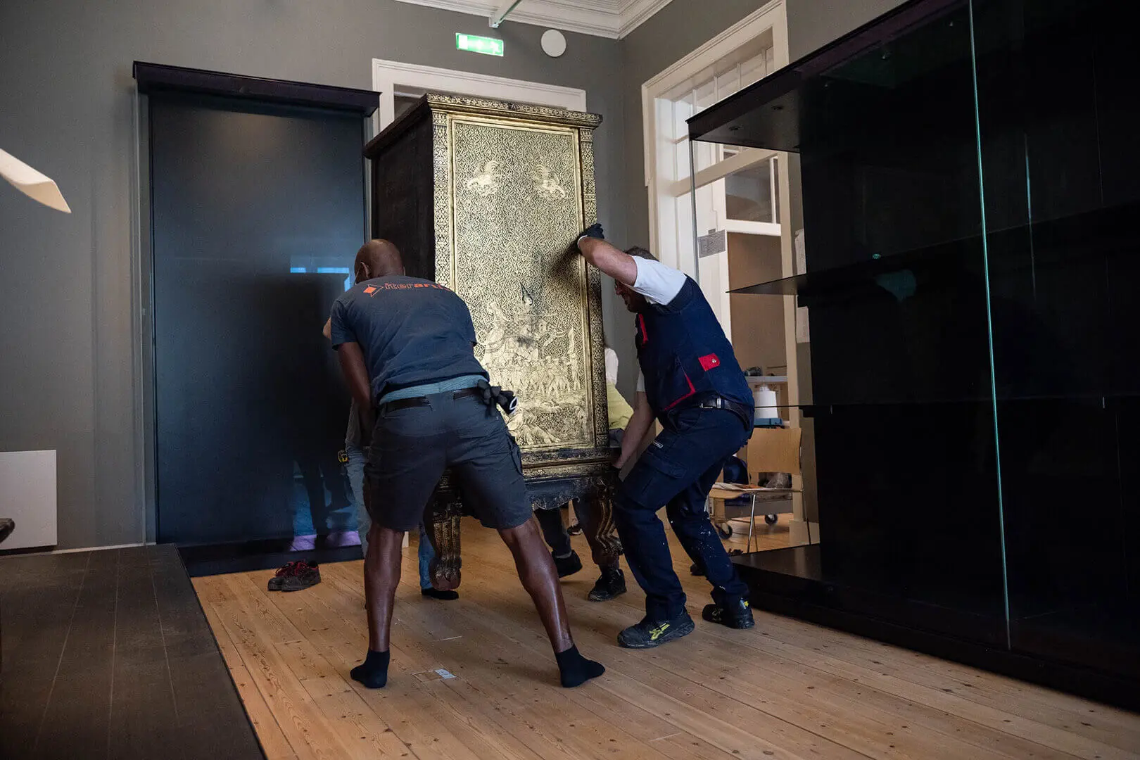 Two technicians moving a gilded sutra cabinet next to the display cases