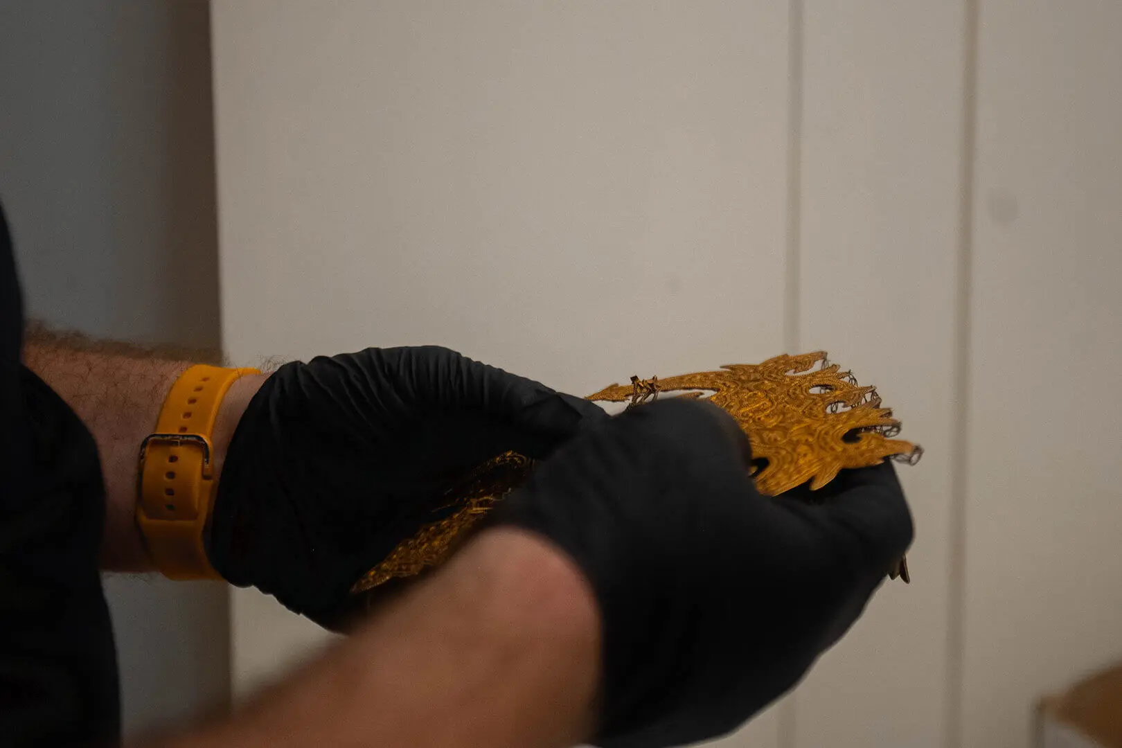 Black-gloved hand holding a gilded piece of goldsmith’s work