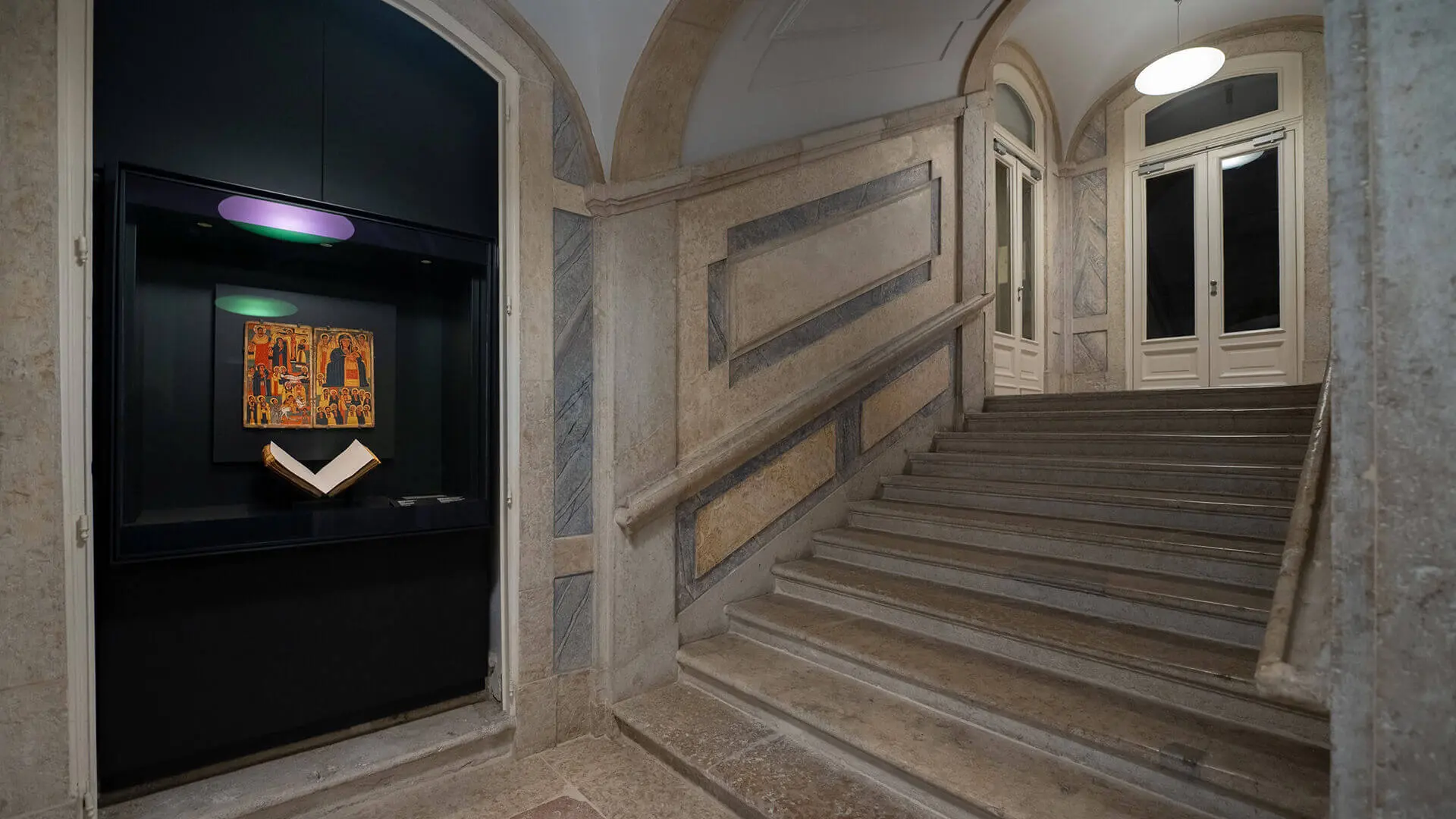The museum staircase, with a showcase holding an open book and a painting