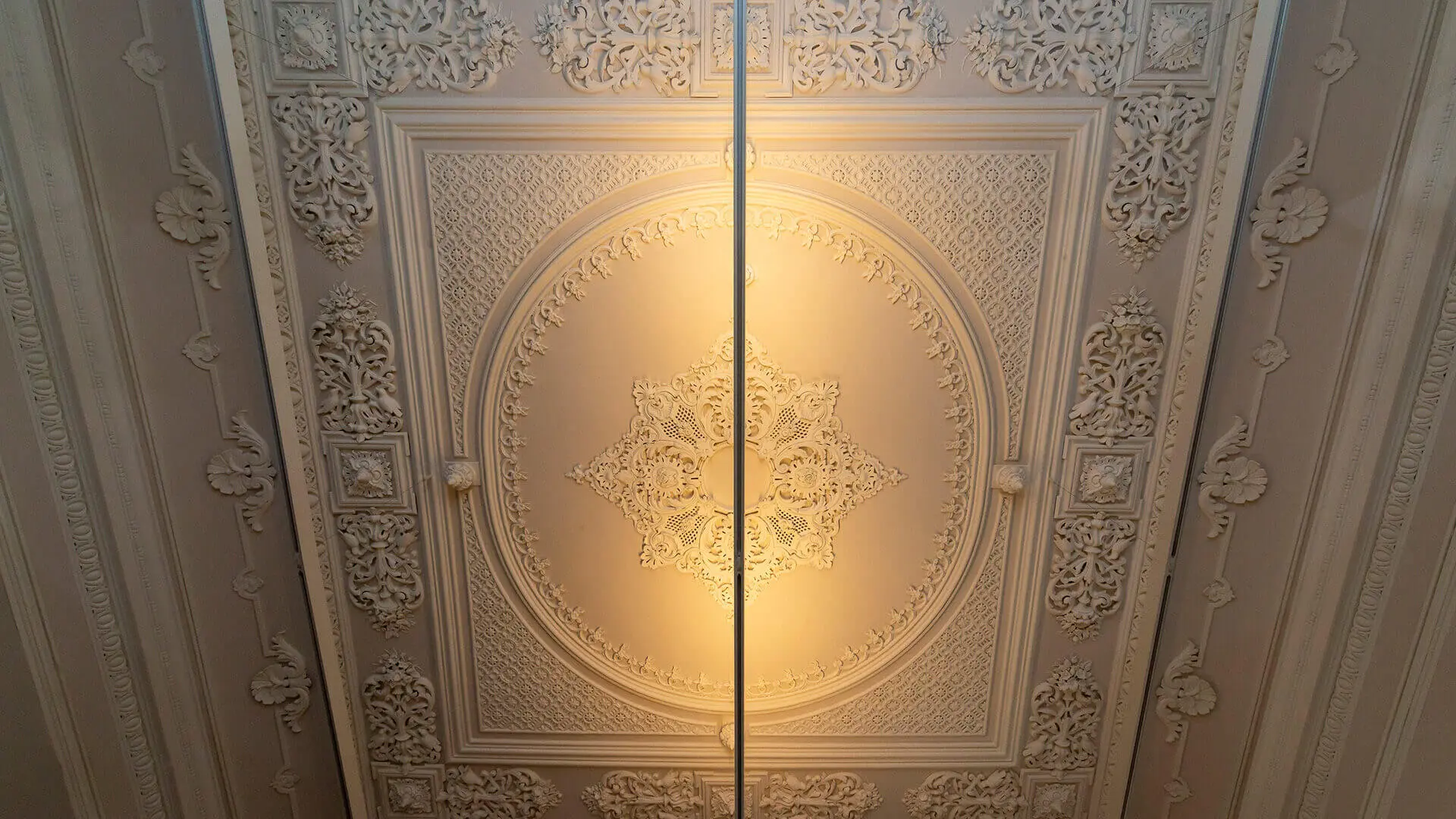 Ornate plaster ceiling with a lit central panel, inside the museum