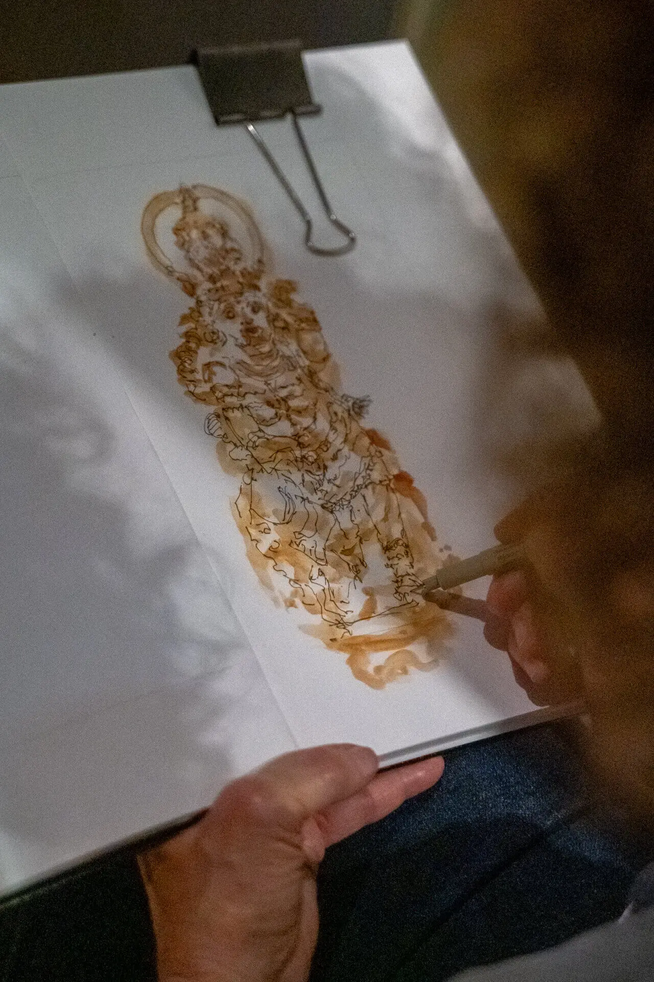 Pormenor de um desenho a aguarela de uma figura, num bloco preso com uma mola