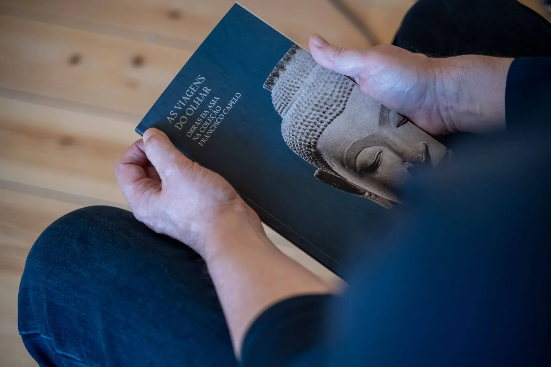 Mãos a segurar o livro «As Viagens do Olhar», com uma cabeça de Buda na capa