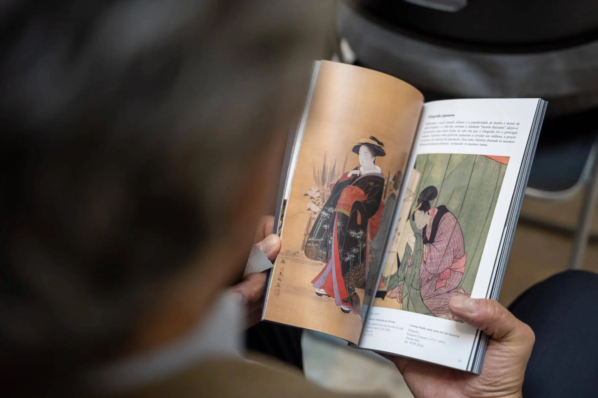 Homem a folhear o Roteiro, aberto numa página com duas pinturas japonesas