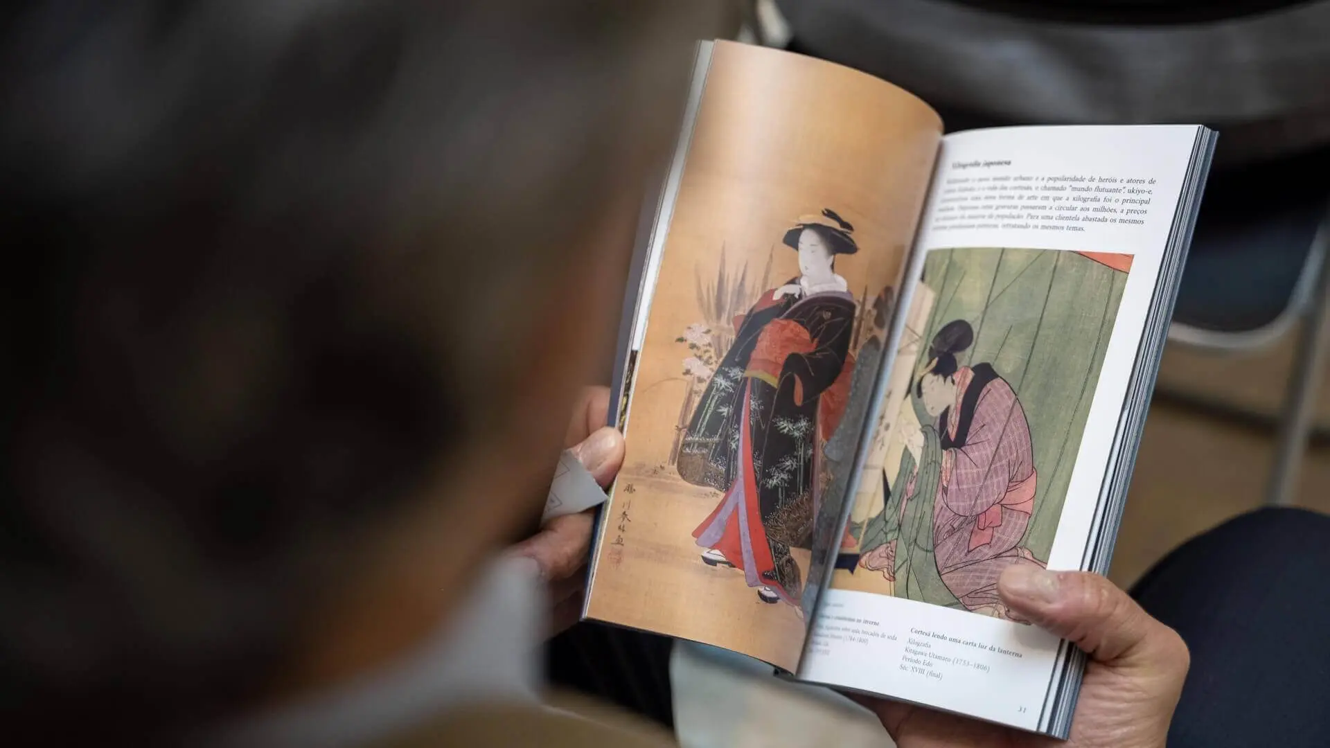 Homem a folhear o Roteiro, aberto numa página com duas pinturas japonesas