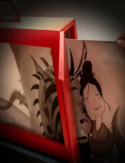 Illustrations from “The Dragon of Akimi” in a red-framed kamishibai theatre: a dragon and a smiling figure