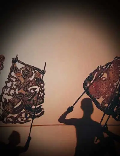 Two shadow puppets and the shadows of their puppeteers on a wall