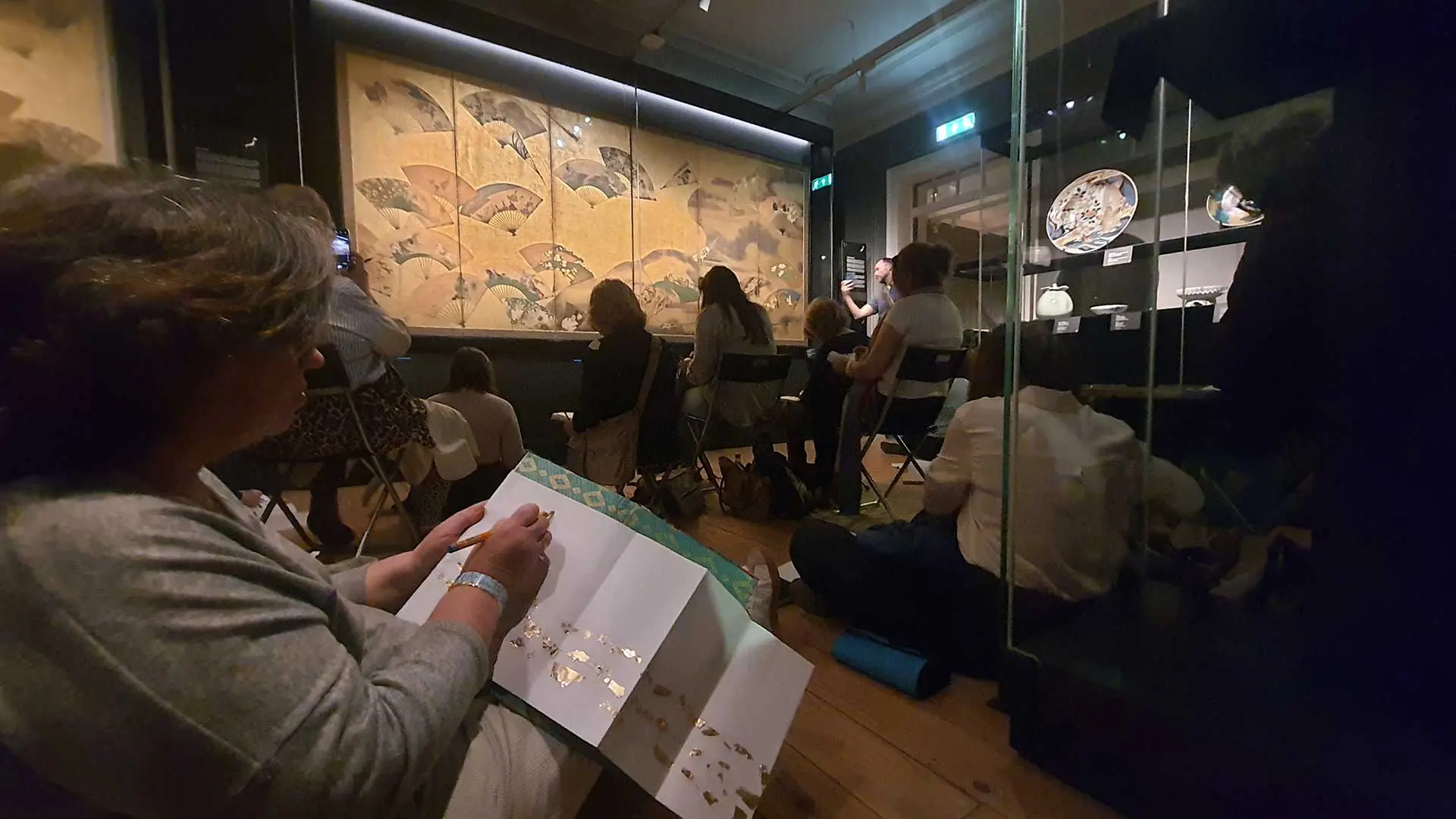 Participantes do workshop sentados a desenhar diante de um biombo japonês