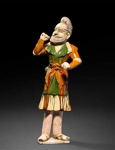 Estatueta de um homem barbudo de pé, com roupa vidrada a verde, castanho e creme, sobre fundo preto